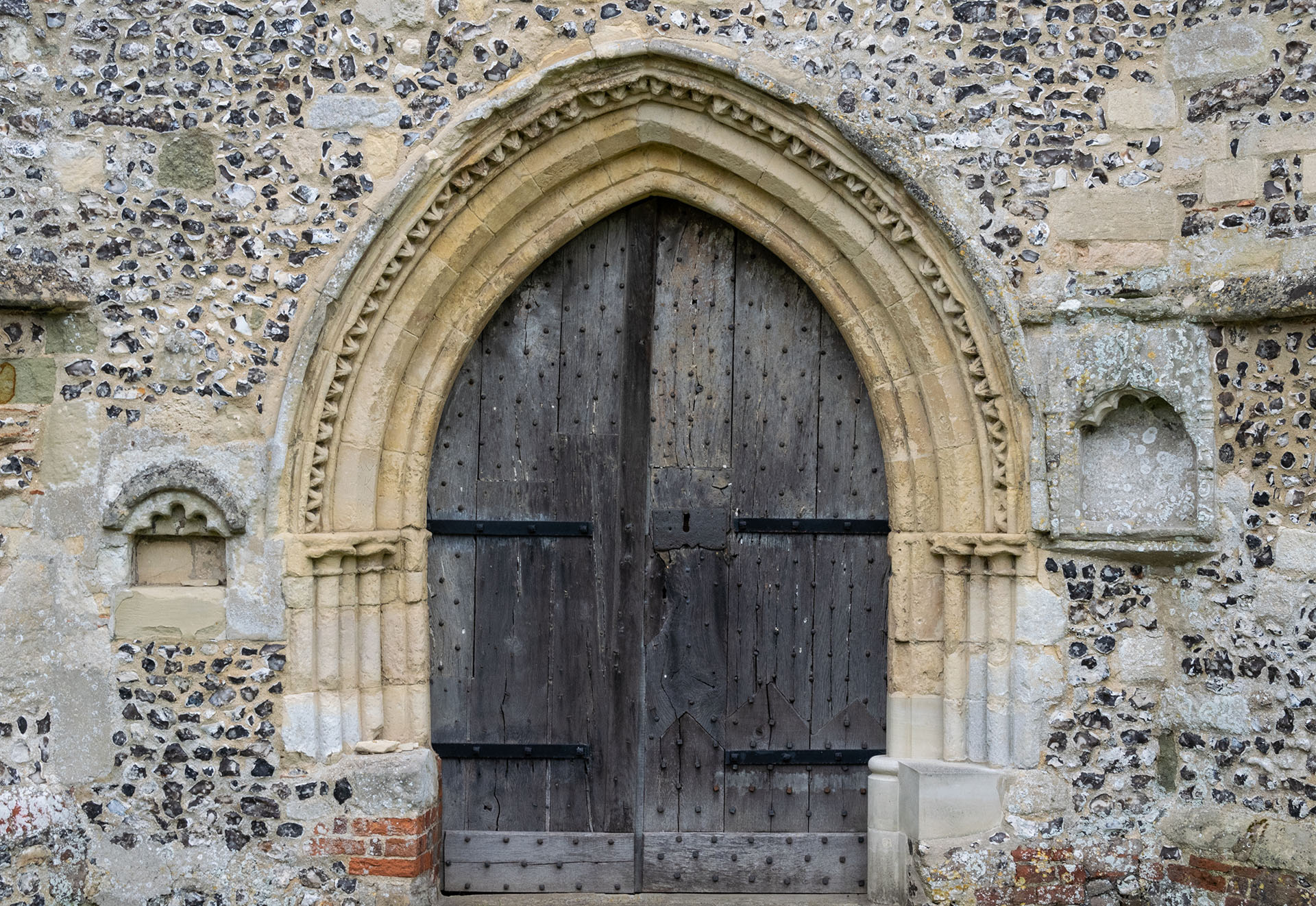 The pretty door of Broughton church, in Early English style, set into flint walls